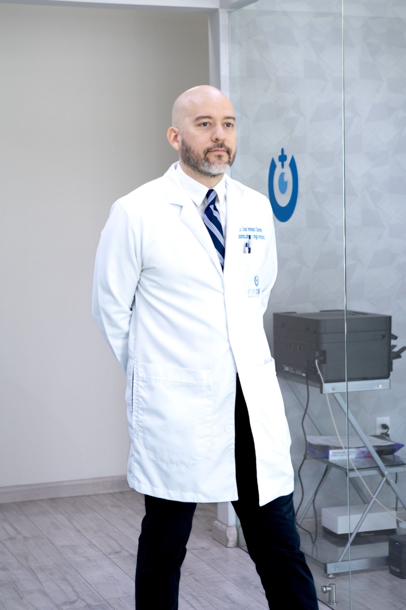 El Dr. César Hernández Chavarría con bata blanca junto al logotipo de EyeCare