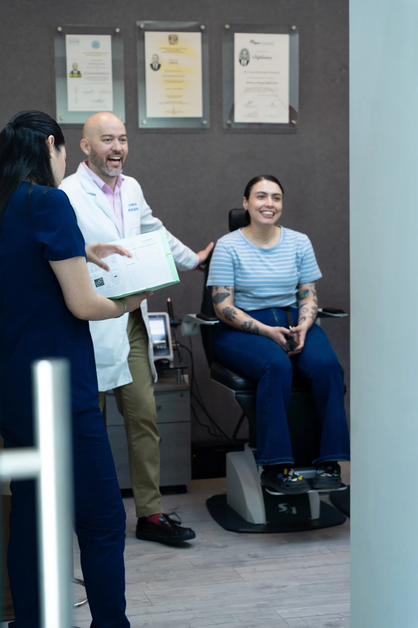 El Dr. Hernández conversa con una paciente frente a la pared de diplomas