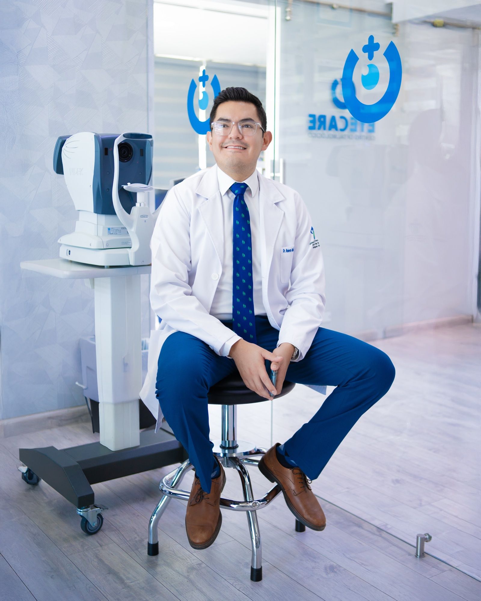 El Dr. Roberto Cervantes Drago, con bata blanca, sentado junto al autorrefractómetro en EyeCare