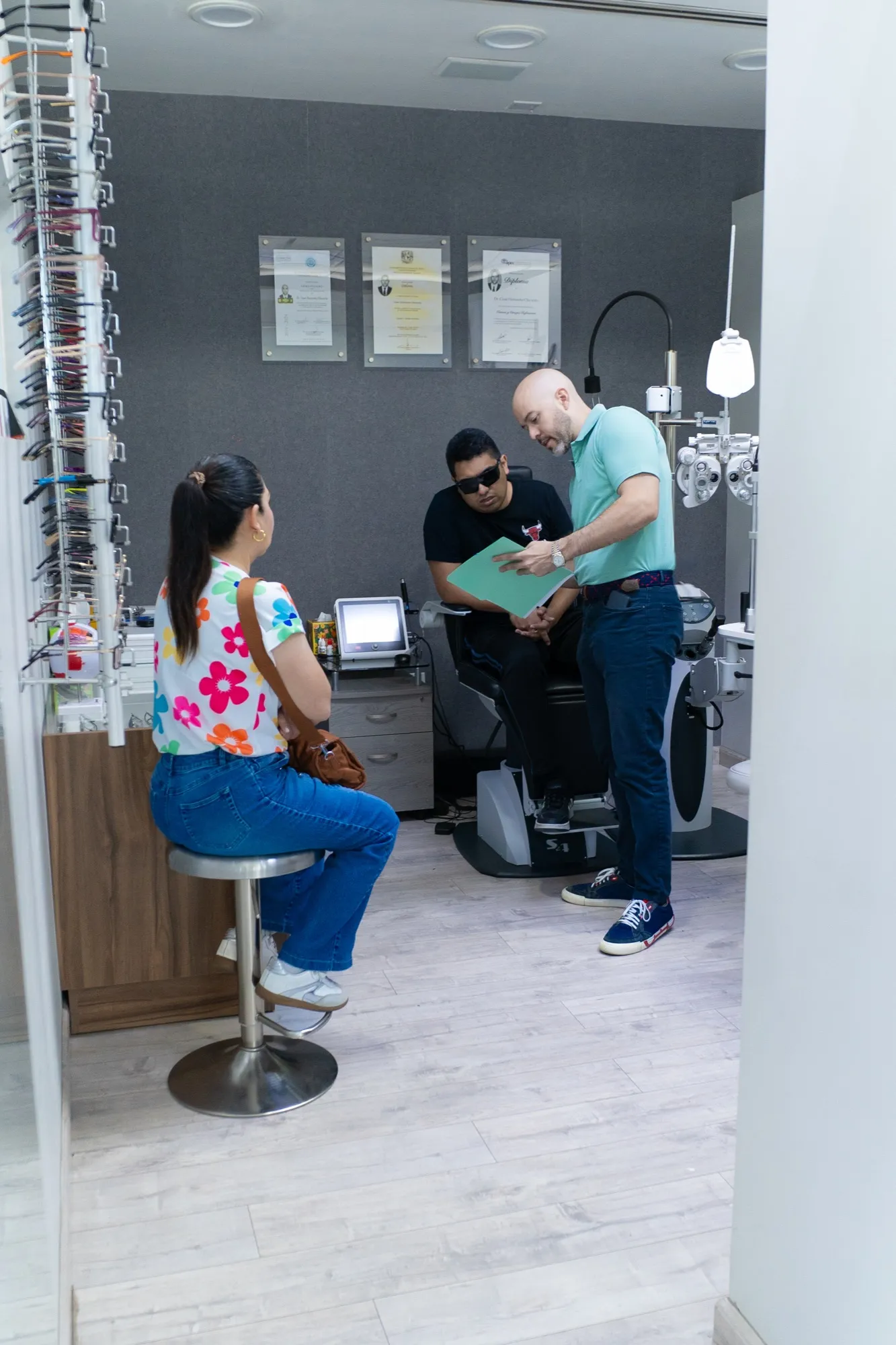 Exhibidor de armazones en el área de óptica de EyeCare, con una familia eligiendo lentes